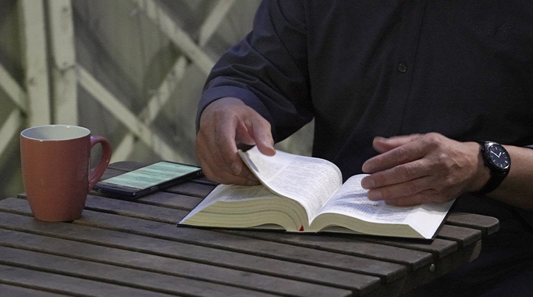 Osoba siedzi przy stole z filiżanką i Biblią