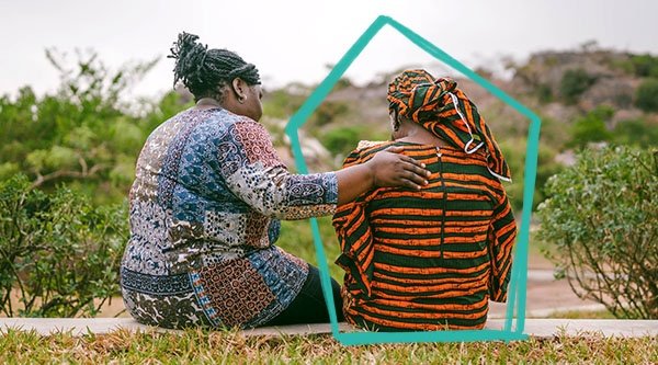 Afrykańska kobieta modli się przed zielonym krajobrazem za inną kobietę.