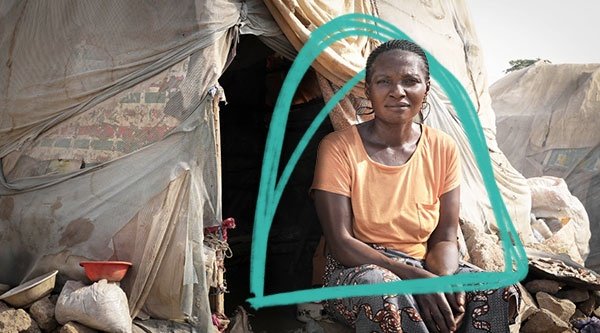 Afrykańska kobieta siedzi przed namiotem w obozie dla uchodźców.